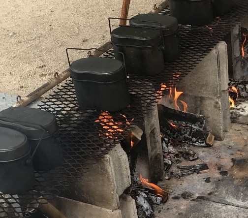 焚き火の上に吊るした飯ごうでご飯を炊いている様子