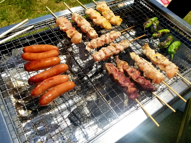 炭火の網の上で焼かれる焼き鳥とウインナー。火の前は真夏だと汗だくになる