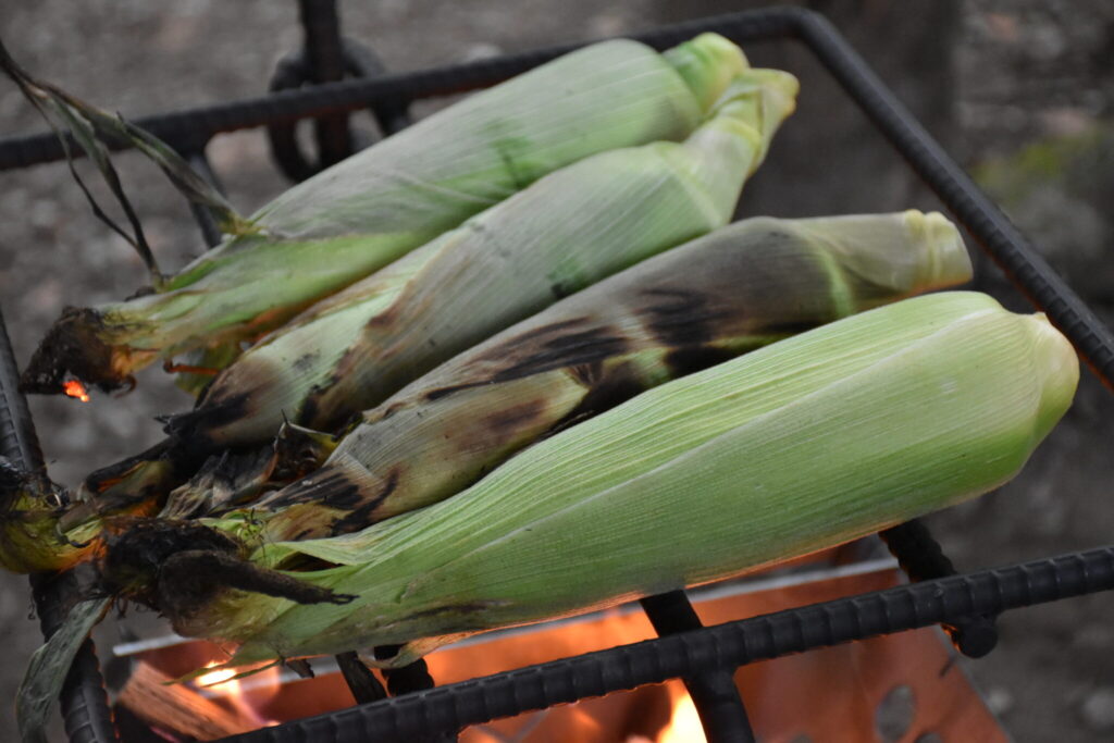 皮付きのままBBQの網の上で焼かれているとうもろこし