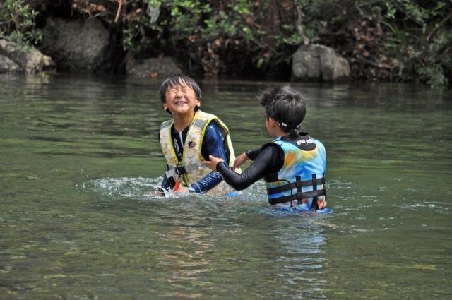 ライフジャケットを着て川で遊ぶ子ども2人