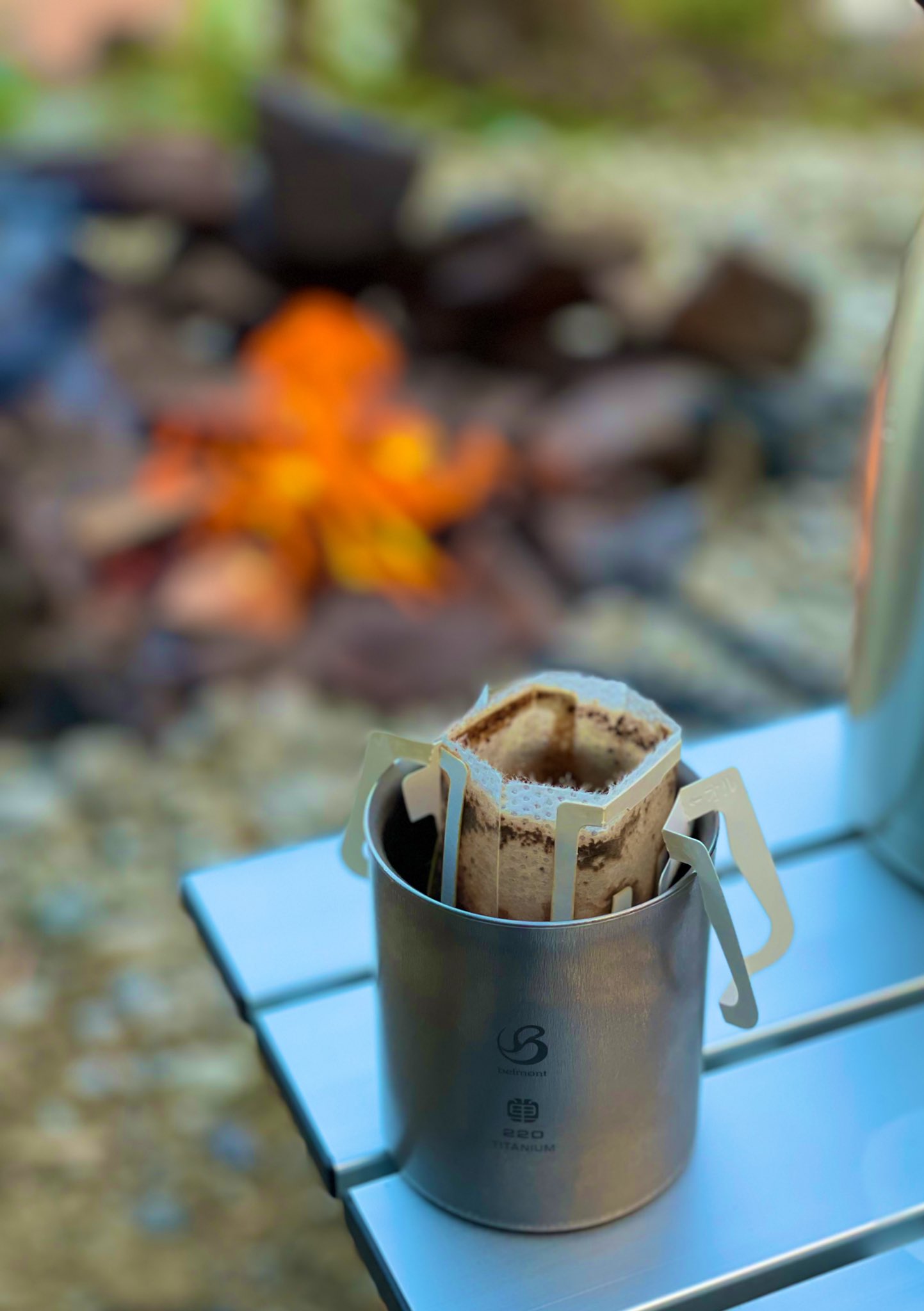 焚き火のそばでチタンマグに注いだコーヒー