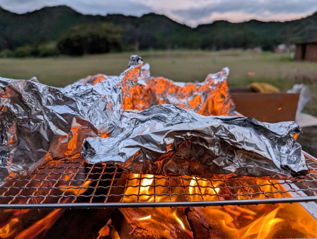 焚き火の網の上でアルミホイルの包み焼きを温めている様子