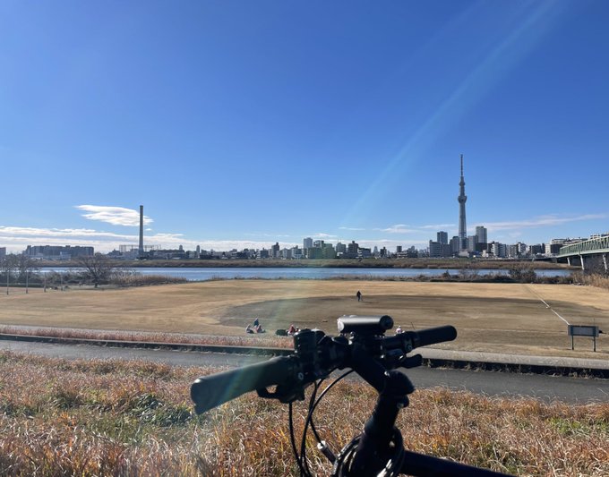 冬枯れの河川敷でひと休みするECoのクロスバイク（XB1）と、遠くのスカイツリー