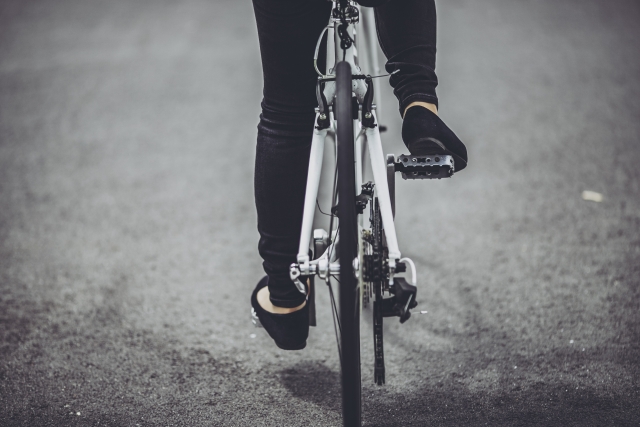 白いロードバイクのペダルに、黒いパンツと革靴の足を乗せて走る通勤の後ろ姿