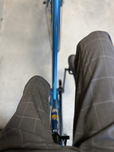 青いクロスバイクにまたがって見下ろした、グレーのチェック柄スラックスのひざ