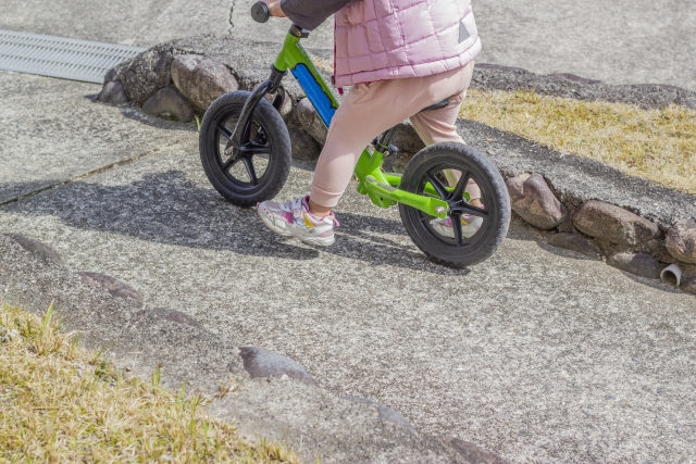 ペダルなし自転車にまたがり、足で地面を蹴って進む子ども