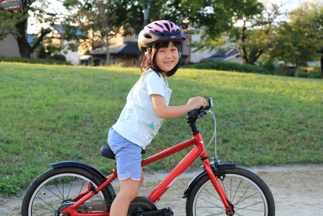ヘルメットをかぶって、公園で自転車に乗る女の子