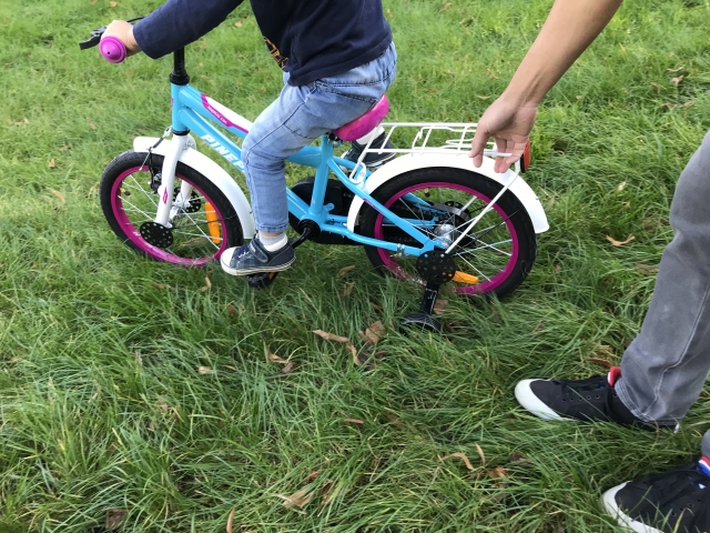 補助輪の付いた子ども用自転車と、後ろで支える大人の手