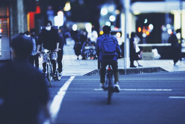 夜の街の車道を、リュックを背負って自転車で走る通勤の人の後ろ姿