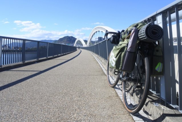 グリーンのパニアバッグとマットを積んだ自転車と、アーチ橋の歩道