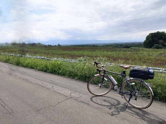 リアキャリアの上にバッグを載せた自転車と、田園の道